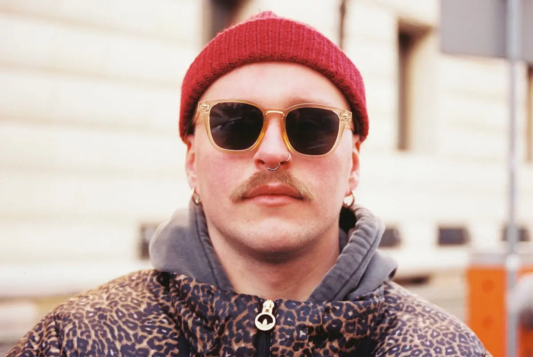 Man with sunglasses and a red beanie smiles.