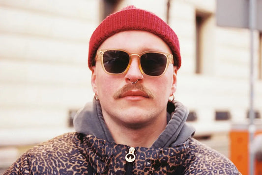 Man with sunglasses and a red beanie smiles.