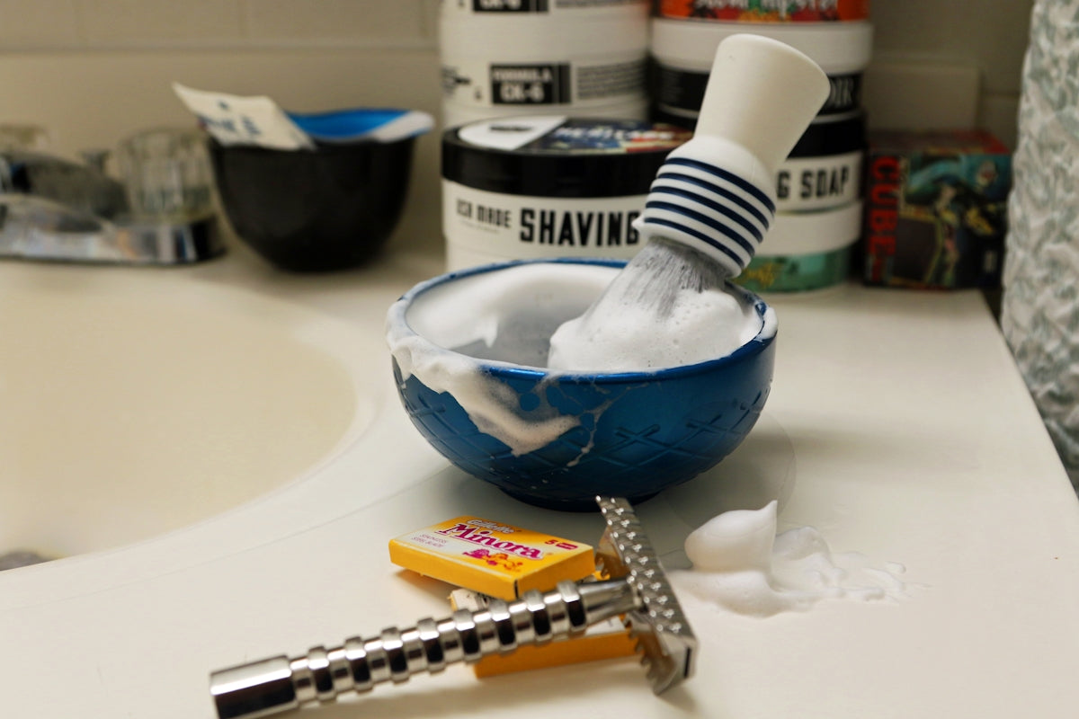Shaving brush and bowl with lather and razor on sink. Image